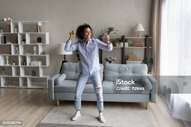 Full length African American woman in headphones dancing, holding smartphone