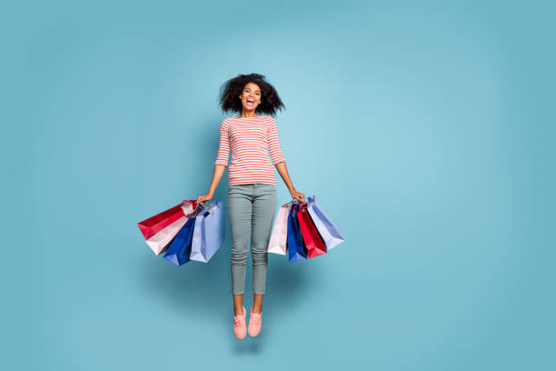 Full length body size photo of stretching jumping excited crazy rejoicing girl black friday packages in striped t-shirt trousers pants footwear isolated over blue pastel color background Full length body size photo of stretching jumping excited crazy rejoicing girl black friday packages in striped t-shirt trousers pants, footwear isolated over blue pastel color background black friday shoppers stock pictures, royalty-free photos & images