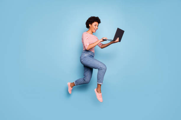 Full length body size side profile photo of pretty cheerful cute nice charming youngster typing before laptop wearing jeans denim striped shirt isolated pastel color blue background Full length body size side profile photo of pretty cheerful cute nice charming, youngster typing before laptop wearing jeans denim striped shirt isolated pastel color blue background jumping stock pictures, royalty-free photos & images