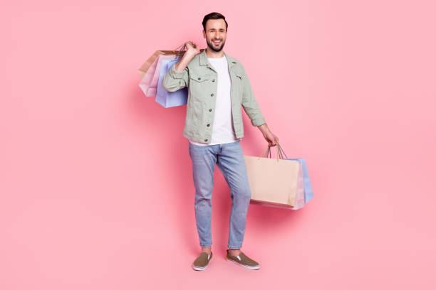 Full length body size view of attractive cheerful guy holding in hands bags presents occasion isolated over pink pastel color background stock photo