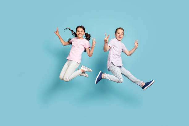 Full length body size view of her she his he nice attractive small little cheerful cheery friends friendship kids jumping showing v-sign having fun isolated over blue pastel color background Full length body size view of her she his he nice attractive small little cheerful cheery, friends friendship kids jumping showing v-sign having fun isolated over blue pastel color background boy jumping stock pictures, royalty-free photos & images