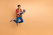 Full length body size view of his he nice attractive cheerful cheery successful brunet, guy jumping in air using laptop home-based job isolated over beige color pastel background