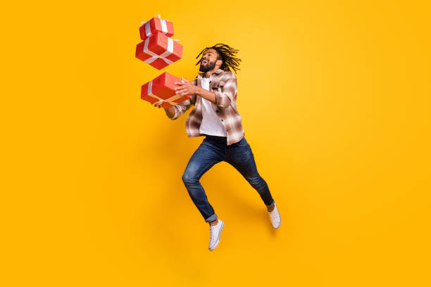 Full length body size view of nice cheerful guy jumping throw drop falling giftboxes isolated over bright yellow color background stock photo