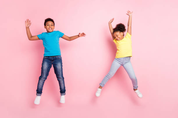 Full length body size view of two attractive cheerful kids jumping having fun isolated over pink pastel color background stock photo