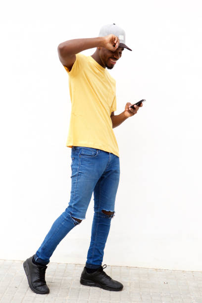 Full length cool young black with cellphone against white wall stock photo