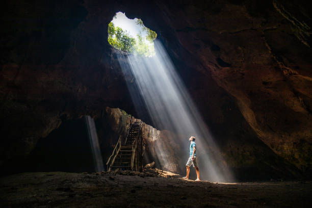 Full length of a carefree man looking at sunbeam entering the cave. stock photo