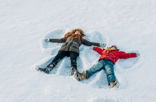 High angle view of sisters making snow angels. Full length of girls are lying on snow. They are enjoying during winter.
