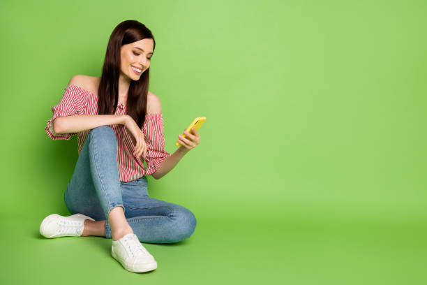 Full length photo of adorable cute young girl hold cellphone connecting parents abroad video call wear denim striped white red shirt uncovered shoulders bright green color background Full length photo of adorable cute young girl hold cellphone connecting, parents abroad video call wear denim striped white red shirt uncovered shoulders bright green color background smart phone green background stock pictures, royalty-free photos & images