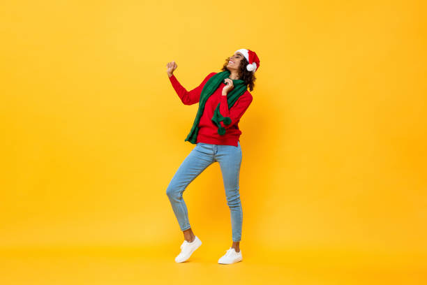 Full length portrait of fun happy woman in Christmas attire dancing on isolated yellow studio background stock photo