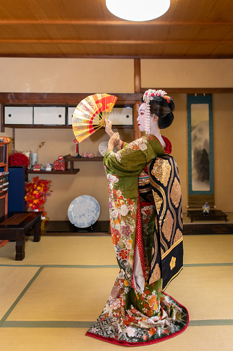 Young female tourist visiting Kyoto and experiencing Maiko (Geisha in training) makeover. Wearing traditional Japanese 'Maiko' style kimono with special white face makeup and walking around beautiful Gion district in Kyoto, Japan.