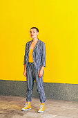 Full length portrait of young short hair beautiful woman in yellow shirt and casual style striped suit standing and looking at camera smiling. indoor studio shot isolated on yellow background.