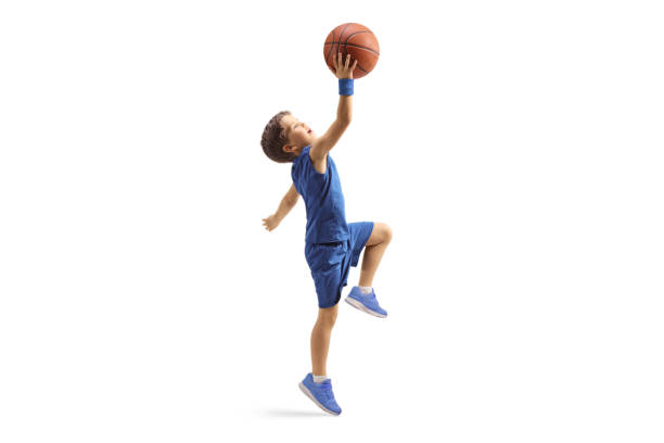 Full length profile shot of a boy in a blue jersey jumping with a basketball stock photo