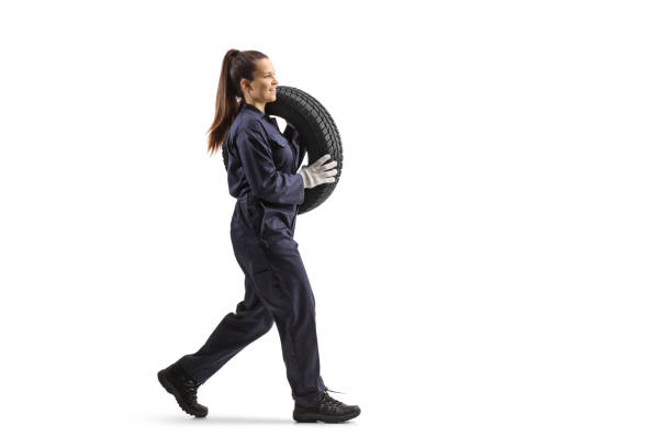 Full length profile shot of a female auto mechanic carrying a vehicle tire and walking stock photo