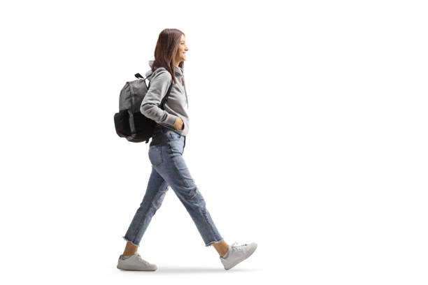 Full length profile shot of a female student in jeans and gray hoodie walking with a backpack stock photo
