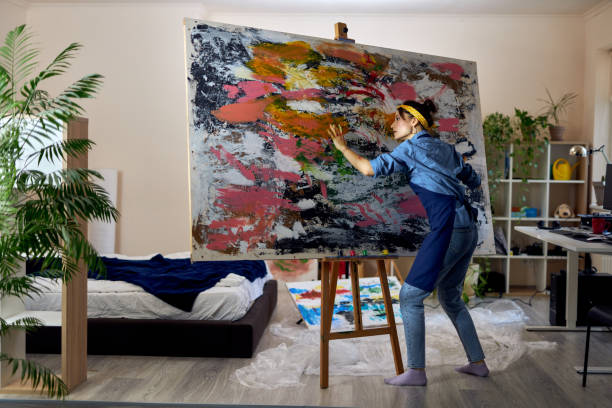Toma de cuerpo entero de pintora inspirada que trabaja en una gran pintura al óleo abstracta moderna, aplicando pintura sobre lienzo con dedos, en el taller de estudio en casa - foto de stock