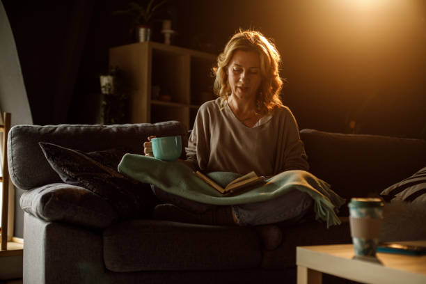Full length shot of woman relaxing on sofa, reading a book and enjoying coffee stock photo