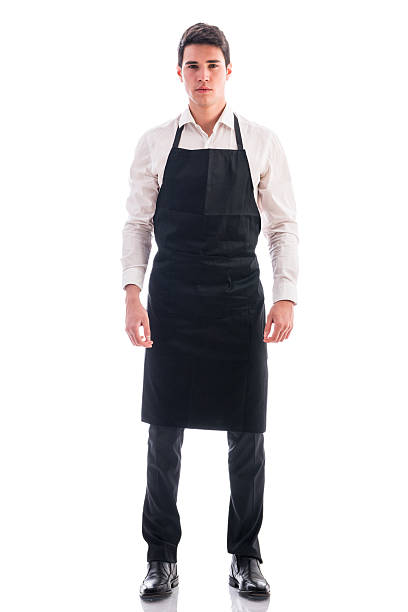 Full length shot of young chef or waiter posing isolated Full length shot of young chef or waiter posing, wearing black apron and white shirt isolated on white background apron stock pictures, royalty-free photos & images