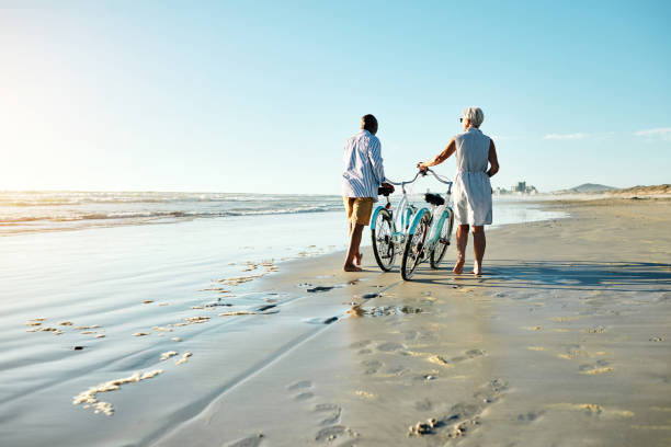 Fun is for everyone Shot of a senior couple riding their bicycles at the beach retirement stock pictures, royalty-free photos & images