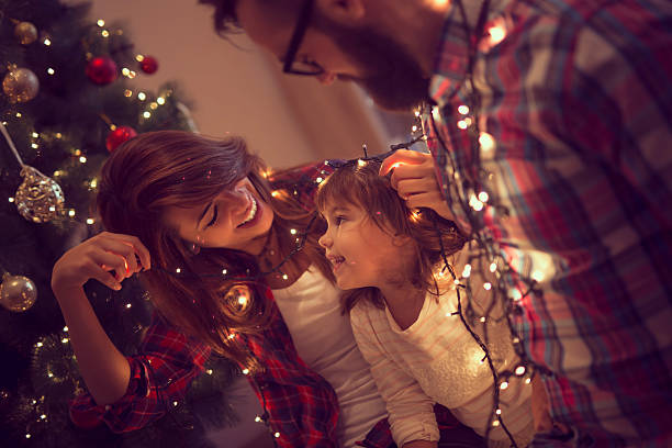 fun with christmas lights - vrouw kerstboom versieren stockfoto's en -beelden