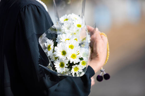 A funeral and visit to a grave of Japan. The woman of the senior worships the ancestral soul in a black mourning dress. I hold white chrysanthemum bunch and beads in a hand. stock photo