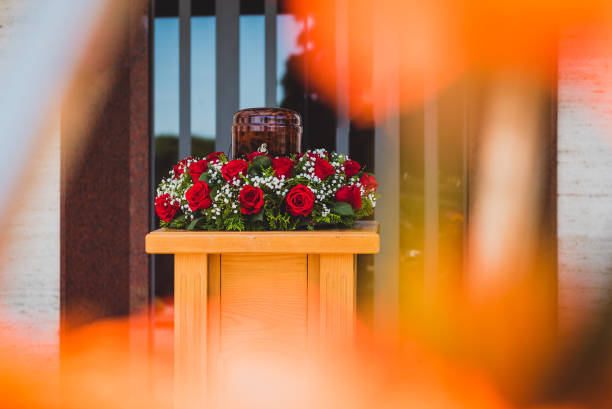 Funerary urn with ashes of dead and flowers at funeral. Funerary urn with ashes of dead and flowers at funeral. Burial urn decorated with flowers at memorial service on a wooden stand, sad and grieving last farewell to deceased person. funerary urn stock pictures, royalty-free photos & images