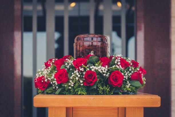 Funerary urn with ashes of dead and flowers at funeral. Funerary urn with ashes of dead and flowers at funeral. Burial urn decorated with flowers at memorial service on a wooden stand, sad and grieving last farewell to deceased person. funerary urn stock pictures, royalty-free photos & images
