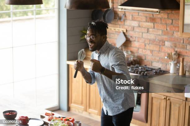 Funny African American man singing into whisk in kitchen