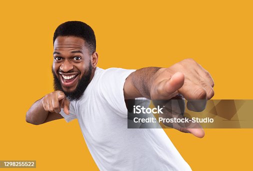 istock Funny african man posing pointing fingers at camera, yellow background 1298255522