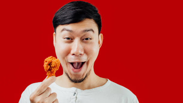 Funny and happy face of Asian man is eating fried chicken deliciously on isolated background. stock photo
