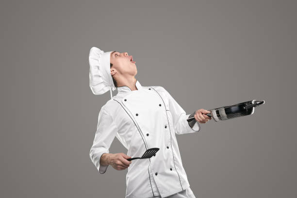 Funny chef with frying pan and spatula looking up stock photo
