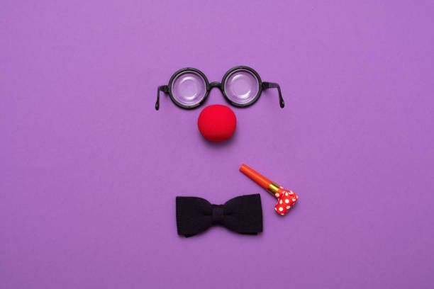 Funny glasses, red clown nose and tie lie on a colored background, like a face. Funny glasses, a red clown nose and tie on a colored background, like a face. Flat lay. Funny costume for the holidays. Anonymous concept. clown's nose stock pictures, royalty-free photos & images