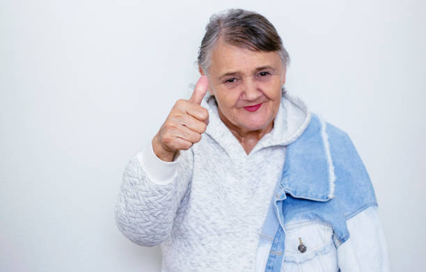 Funny grandma's portraits. An elderly lady makes a hipster gesture with her hand "OK". Fashion hipster woman having fun. Funny moments with a woman's grandmother. Lifestyle and concepts of people stock photo