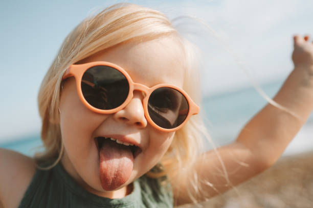 Funny kid sticking out tongue playing outdoor happy emotional child in sunglasses 3 years old baby family vacations stock photo