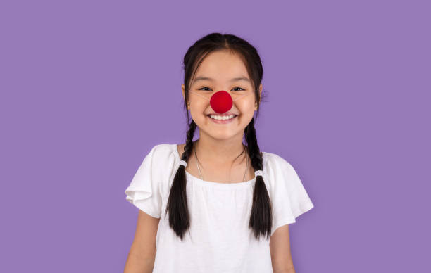 Funny Korean Kid Girl Posing Wearing Clown's Nose, Studio Shot Funny Korean Kid Girl Wearing Clown's Nose Posing Smiling To Camera On Purple Background. Studio Shot clown's nose stock pictures, royalty-free photos & images