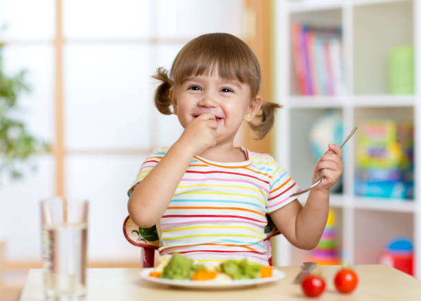 Funny little girl eating healthy food in kindergarten stock photo