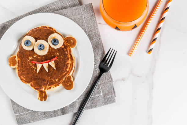 Funny pancakes for Halloween Funny food for Halloween. Kids breakfast pancake decorated like creepy monster, with banana, berries, with pumpkin smoothie juice, white table copy space top view monster fictional character photos stock pictures, royalty-free photos & images