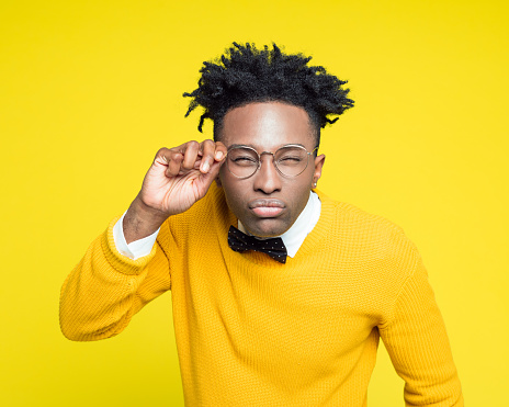 Portrait of nerdy young afro American man wearing yellow sweater and black bow tie staring at camera. Studio shot against yellow background.