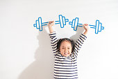 istock Funny Positive strong Asian little toddler kid girl lifting weight against the textured white background. For empowering women, girl power and feminism, sport, education, and creative future Ideas. 1342239447