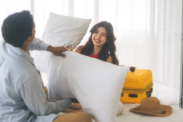 Funny relax of young adult southeast asian couple playing with pillow on bed among holidays travel trip stock photo