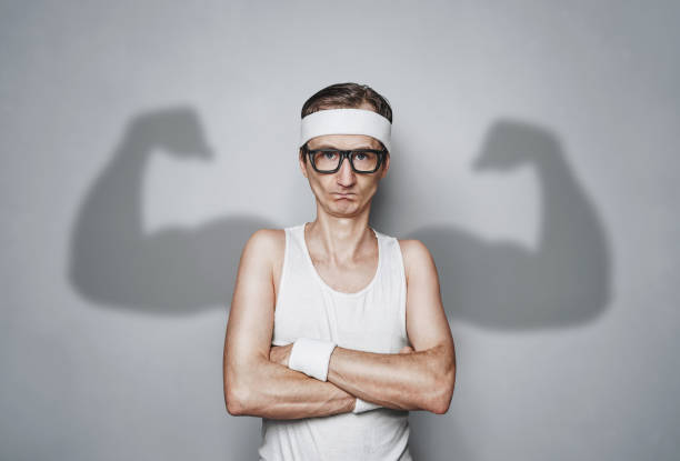 Funny sport nerd with large shadow arms Funny sport nerd with shadow muscle arms over gray wall with copy space male bodybuilders stock pictures, royalty-free photos & images