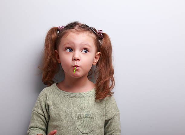 Funny thinking kid girl eating lollipop and looking up stock photo