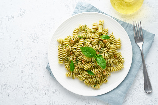 fusili pasta with basil pesto and herbs, italian cuisine, gray stone background, top view
