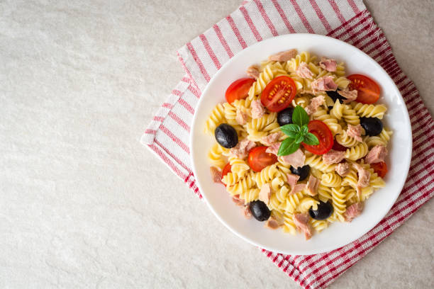 Fusilli pasta salad with tuna, tomatoes, black olives and basil on gray stone background stock photo