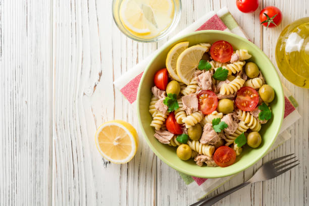 Fusilli pasta salad with tuna, tomatoes, olives and parsley on white wooden background. stock photo