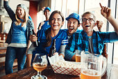 Shot of a group of friends cheering while watching a sports game at a bar