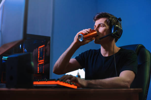 Gamer drinking energy drink to be focused on online computer game at night Cyber sport. Professional cybersport player training or playing online video game on his PC late at night, drinking caffeine energy drink to concentrate, focus on game. Team play. Games addiction energy drink stock pictures, royalty-free photos & images