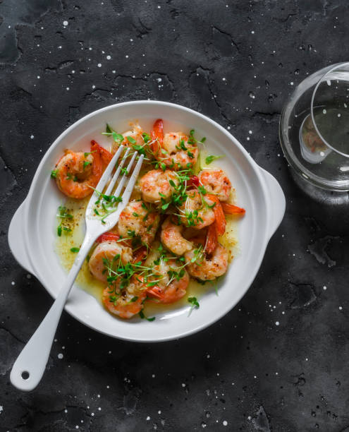 Garlic butter fried shrimp and a glass of white wine on a dark background, top view stock photo