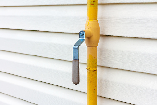 Yellow gas pipe with manual valve on the wall of the house