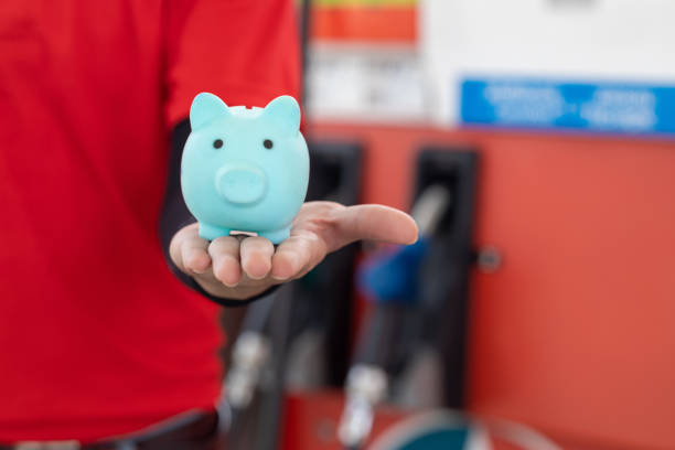 Gas station staff worker with piggy bank for save money from low fuel price, gas costs reduction, cut and saving gasoline drop price concept. stock photo