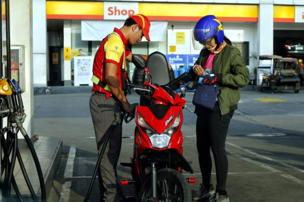 Gasoline station employee refills the fuel tank of a motorcycle for a customer stock photo